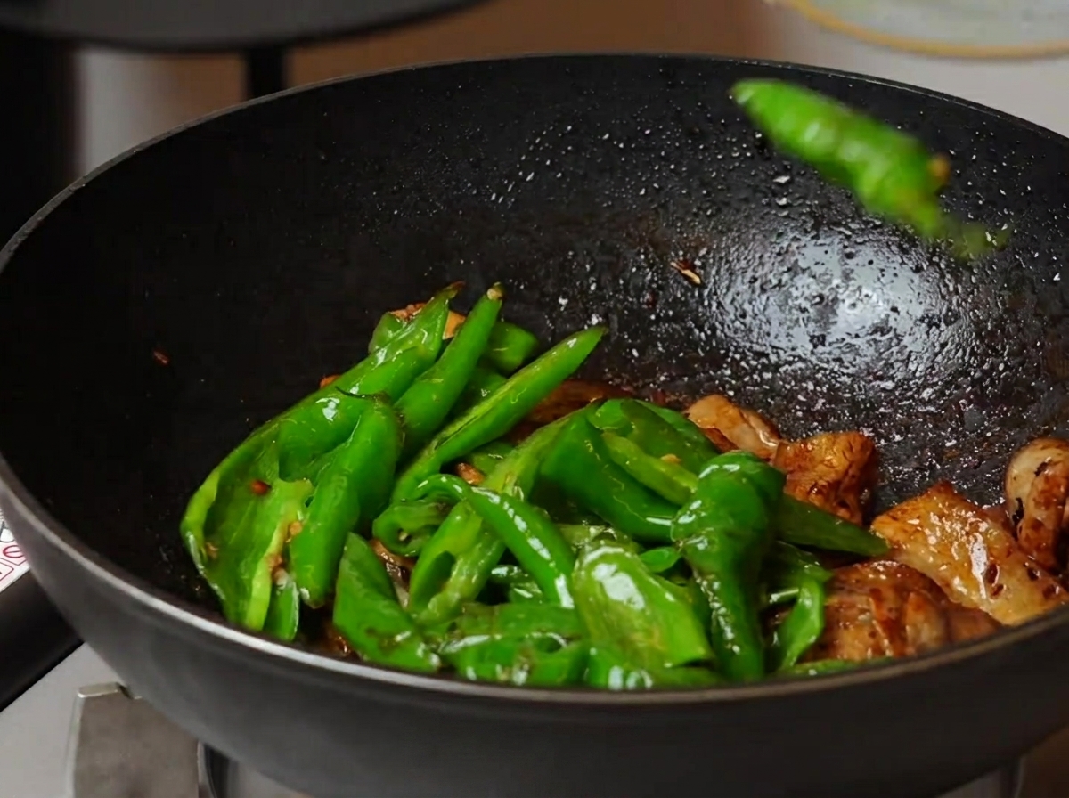 Pimientos tostados mezclándose con la panceta en un wok grande.