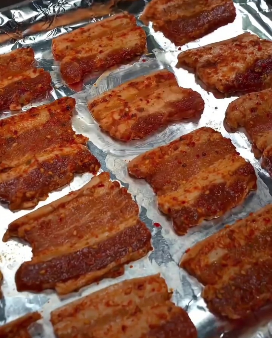 Rociando aceite de cocina sobre las rebanadas de panceta cruda en la bandeja para hornear.