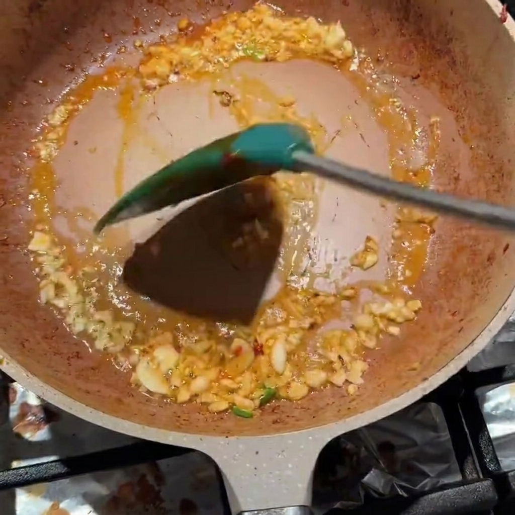 Ajo picado y pasta de frijoles Pixian siendo mezclados en una sartén.