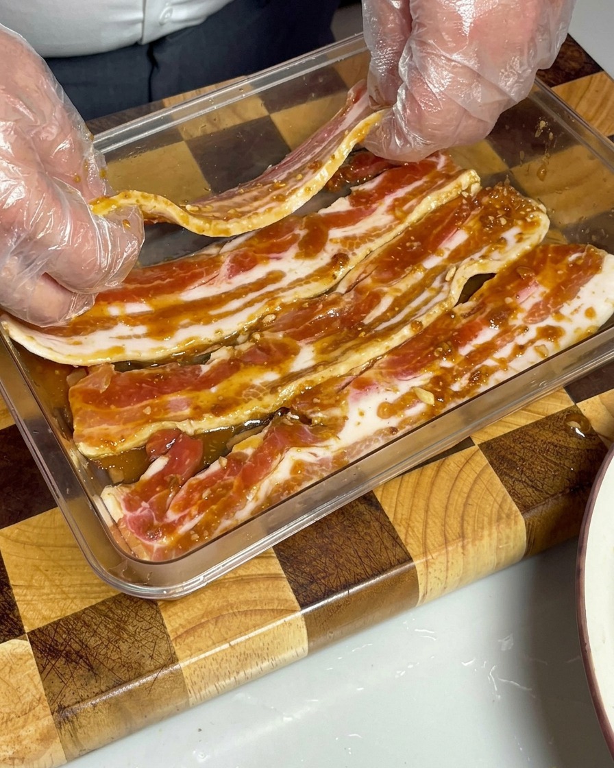 Tiras de panceta de cerdo marinadas dispuestas cuidadosamente en un recipiente transparente, totalmente sumergidas en la salsa de miso marrón.