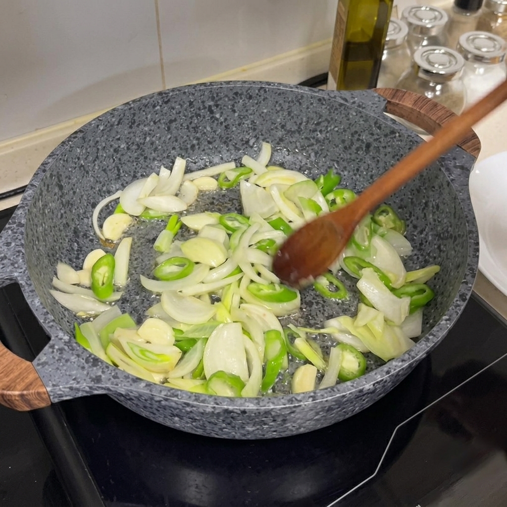 Cebollas, chiles verdes y ajo siendo salteados en una sartén caliente con una cuchara de madera.