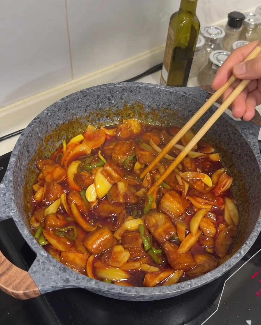El plato final de cerdo salteado picante con carne dorada visible, salsa brillante y un ligero espolvoreado de semillas de sésamo blanco encima.