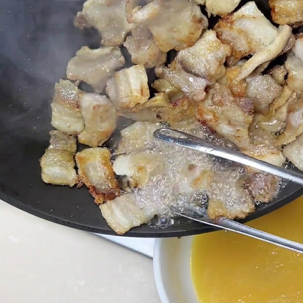 Pinzas sosteniendo tiras de panceta mientras el exceso de grasa dorada se vierte fuera de la sartén.