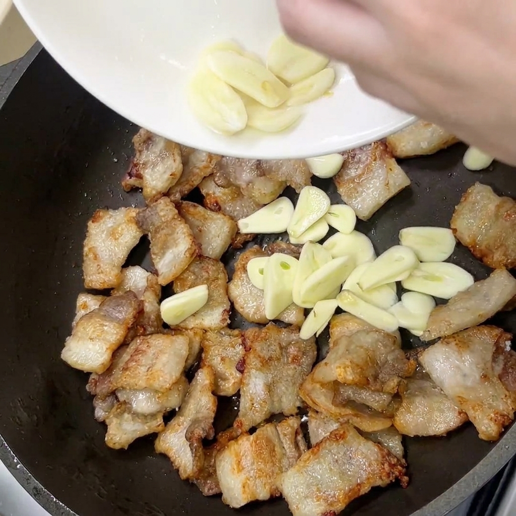 Rodajas de ajo fresco añadidas a la sartén con la panceta de cerdo bien dorada.