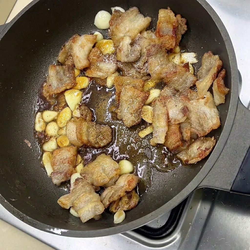 Panceta glaseada y dientes de ajo siendo salteados en la sartén con condimentos sabrosos.