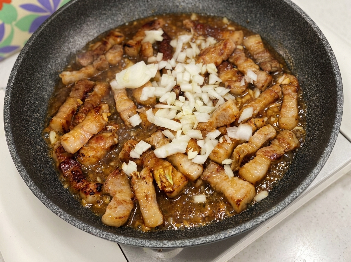 Cebollas blancas troceadas añadidas a una sartén con cerdo y una salsa burbujeante.