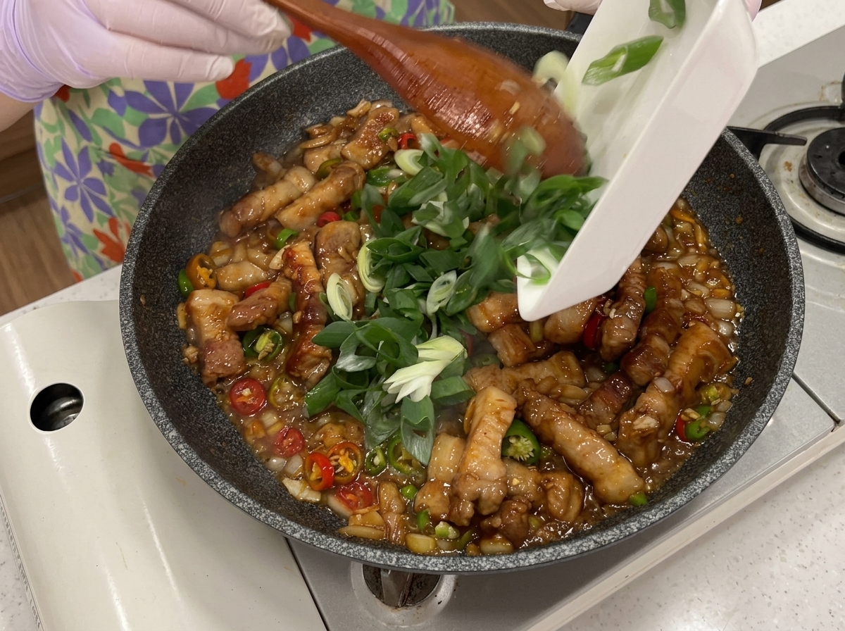 Chiles verdes y rojos junto con cebollino añadidos a la sartén con el cerdo.