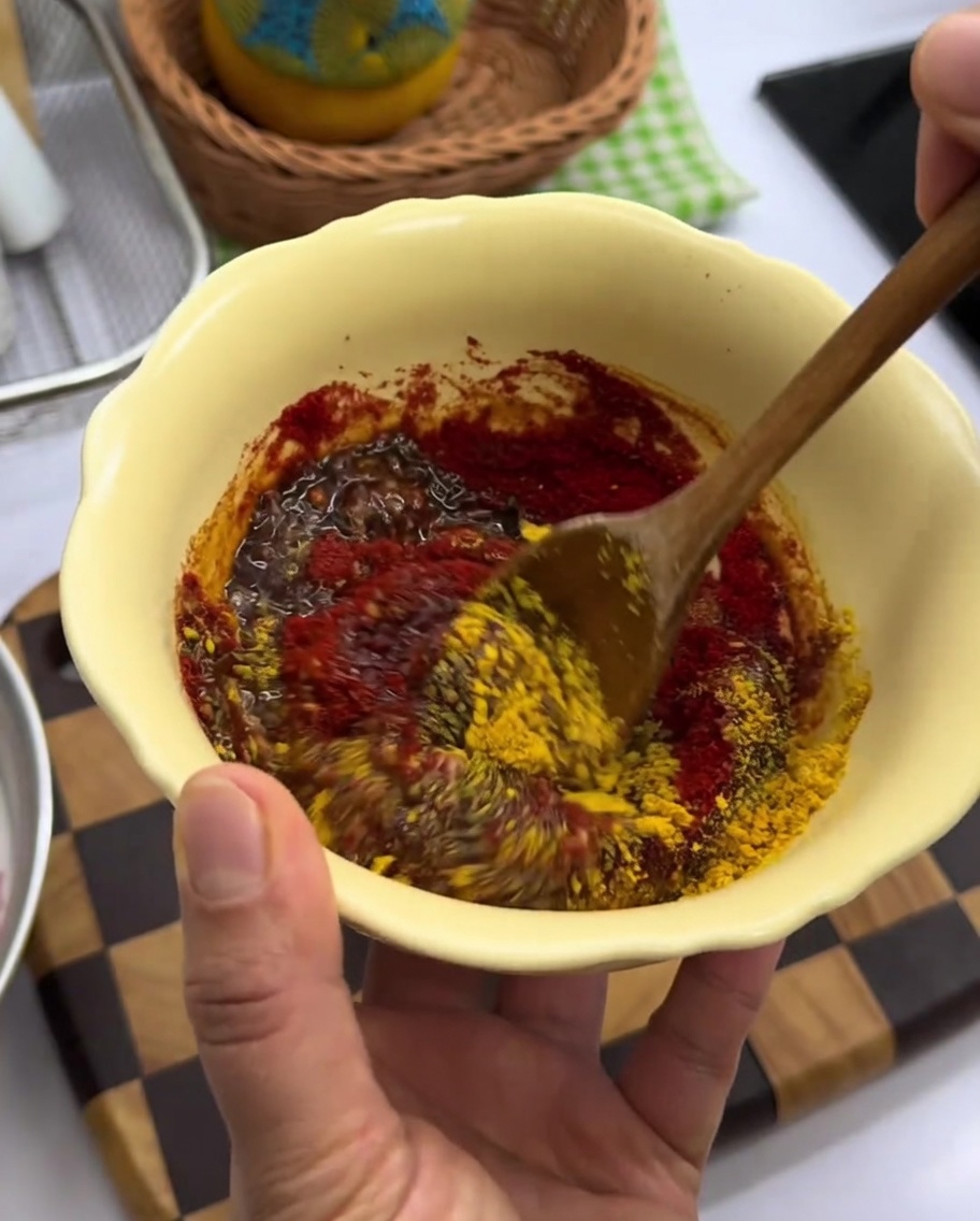 Pasta de especias roja espesa siendo mezclada en un bol amarillo.