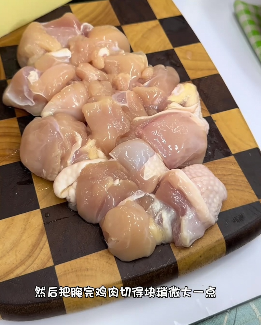 Trozos uniformes de contramuslo de pollo crudo sobre una tabla de cortar de madera.