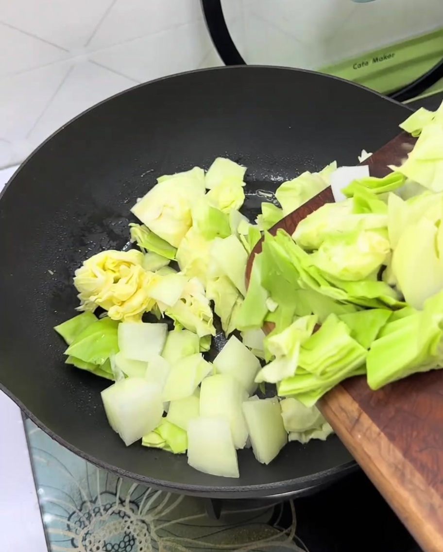 Repollo fresco y cebolla en rodajas añadidos a una sartén vacía.