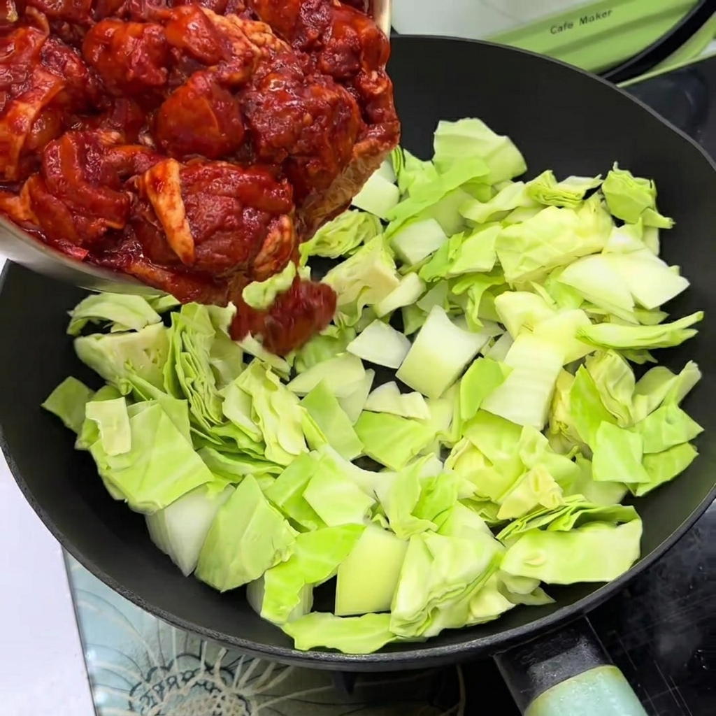 Trozos de pollo marinado colocados sobre repollo y cebollas en una sartén.