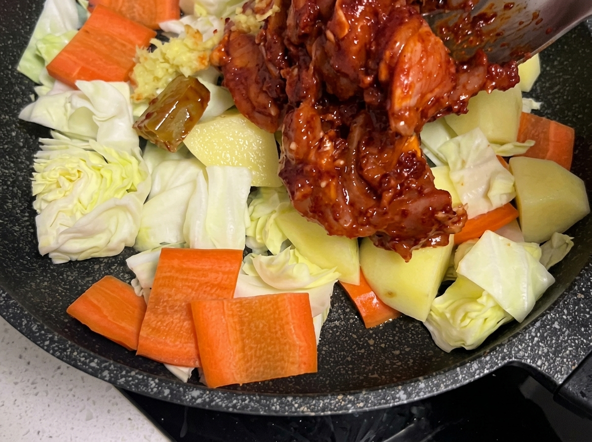 Trozos de pollo marinado siendo colocados cuidadosamente sobre la cama de verduras en la sartén.