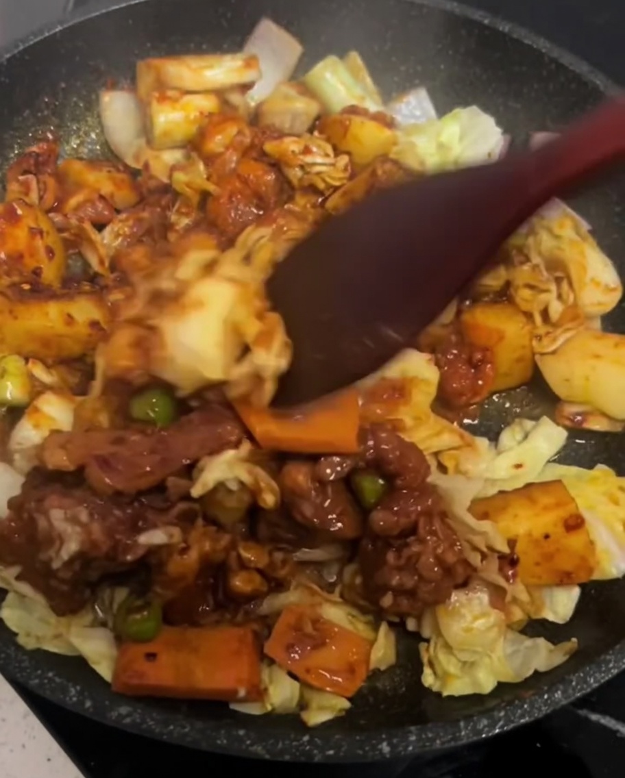 Una espátula mezclando suavemente el pollo y las verduras en una sartén caliente.