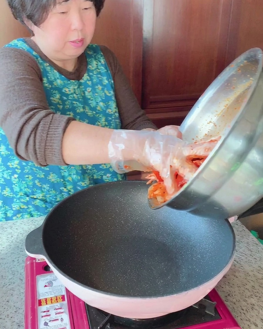 La mezcla marinada de cerdo y calamar se vierte desde un tazón de acero inoxidable a una sartén caliente.
