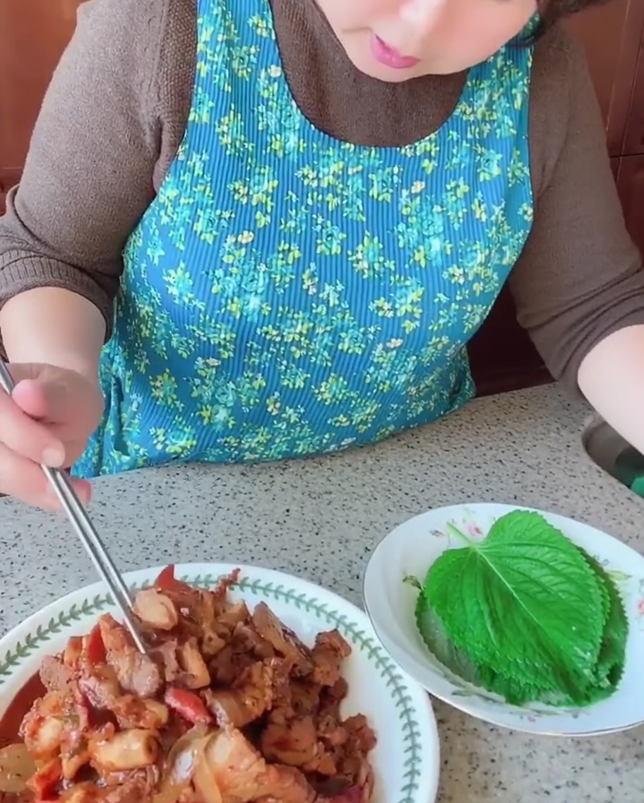Una persona usando palillos para colocar un trozo de panceta y calamar cocidos sobre una hoja verde fresca de perilla.