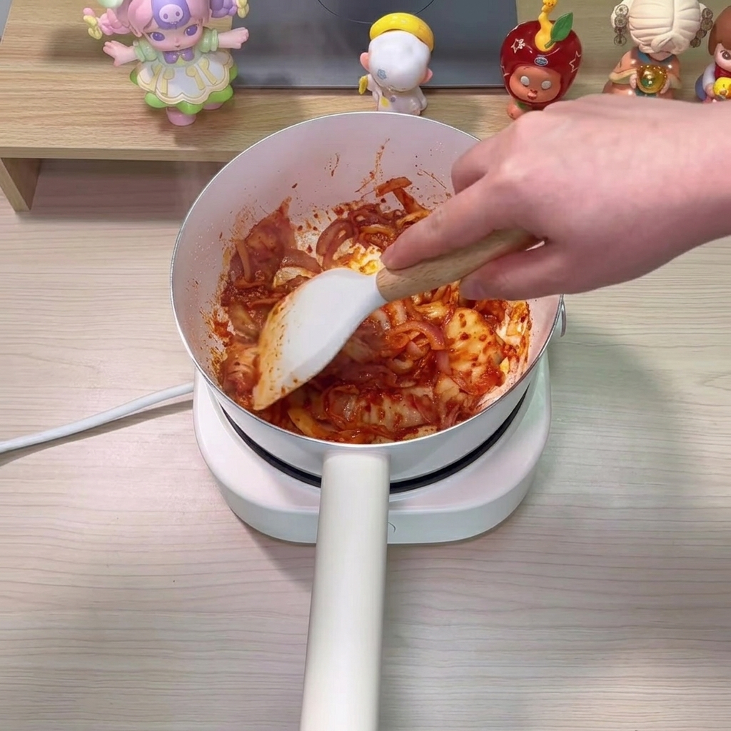 Agua clara vertiéndose en la olla, combinándose con el kimchi y las cebollas salteadas.