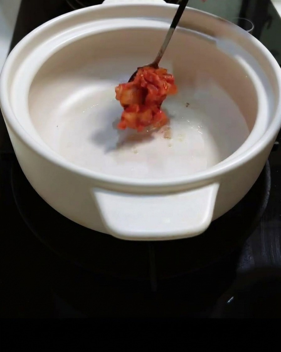 Kimchi picante picado siendo añadido a la olla y removido.