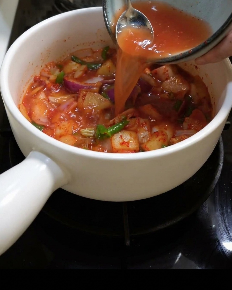 Agua siendo vertida en la olla llena con kimchi y cebollas.