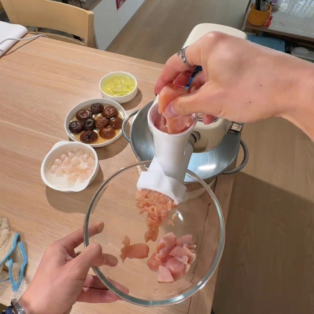 Una mano colocando trozos de pechuga de pollo en un cuenco grande.