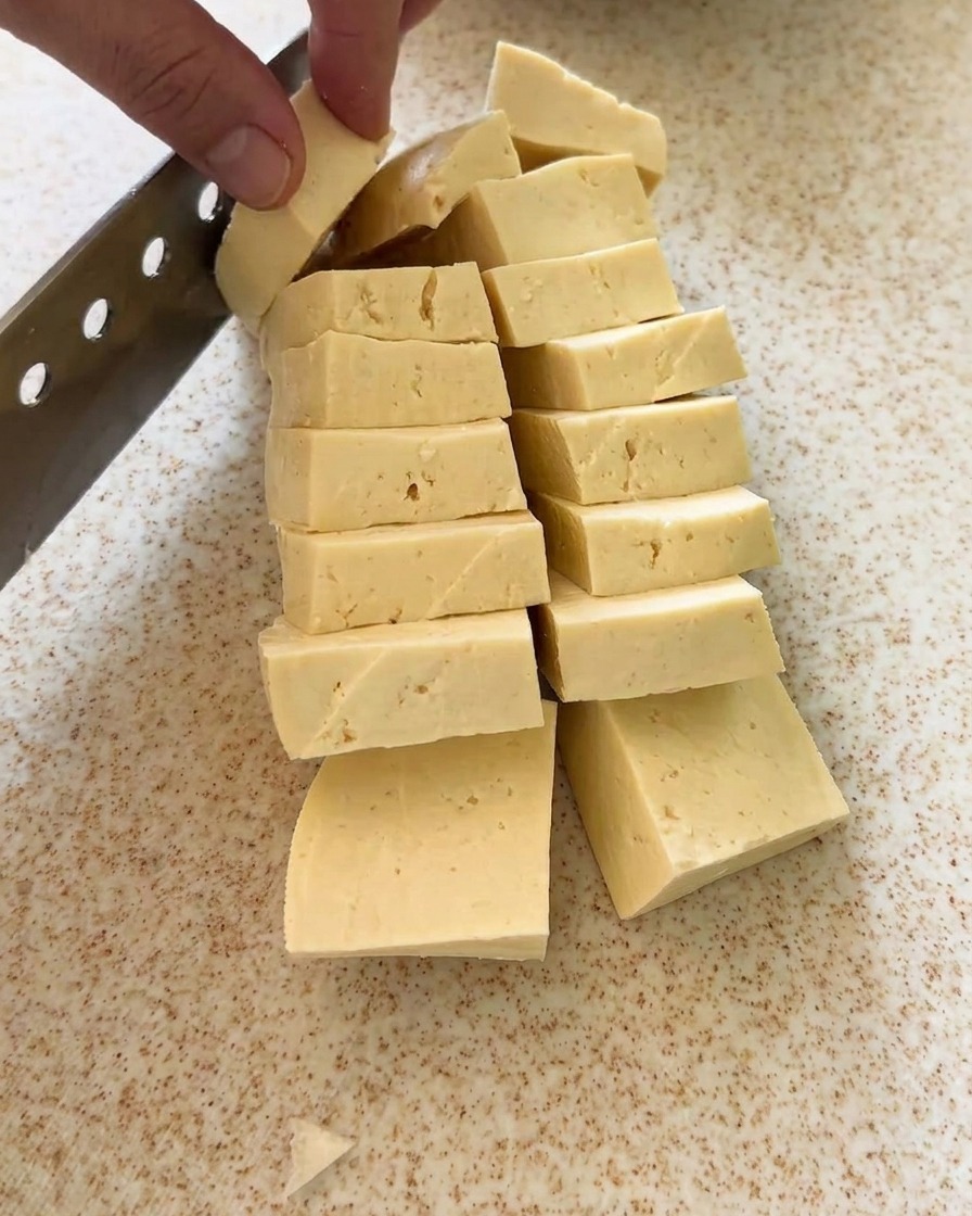 Un bloque de tofu cortado en piezas uniformes sobre una tabla.