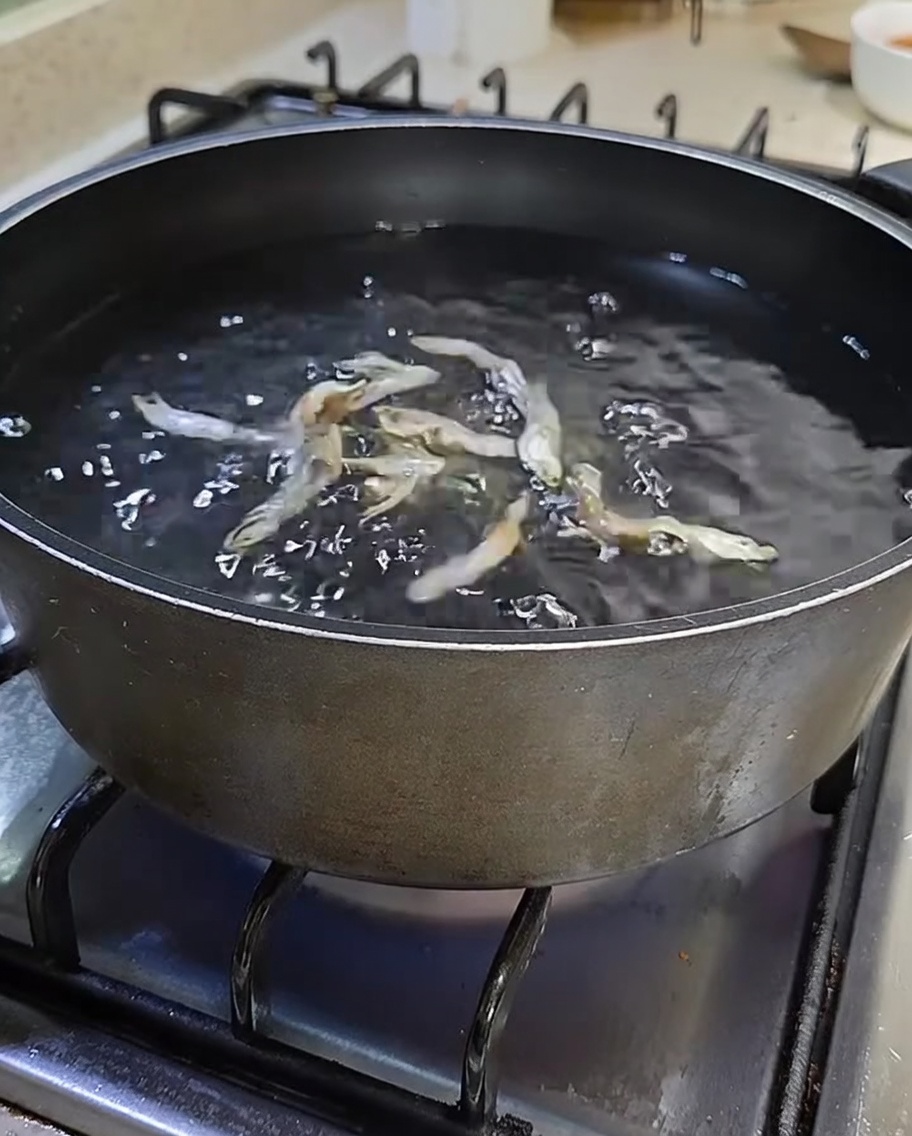 Una olla negra en la estufa llena de agua y anchoas secas.