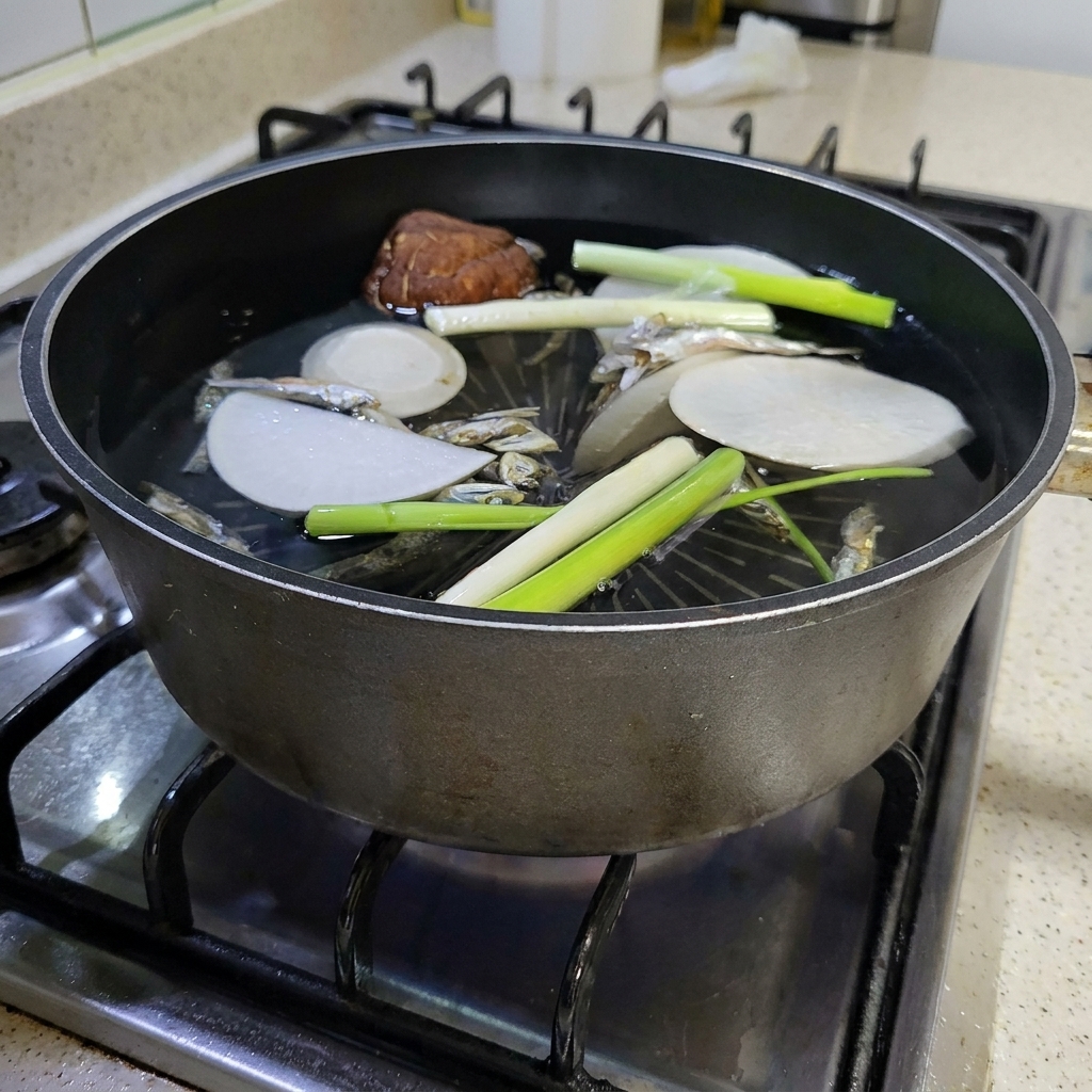 Un trozo grande de alga kombu seca siendo añadido a la olla hirviendo.
