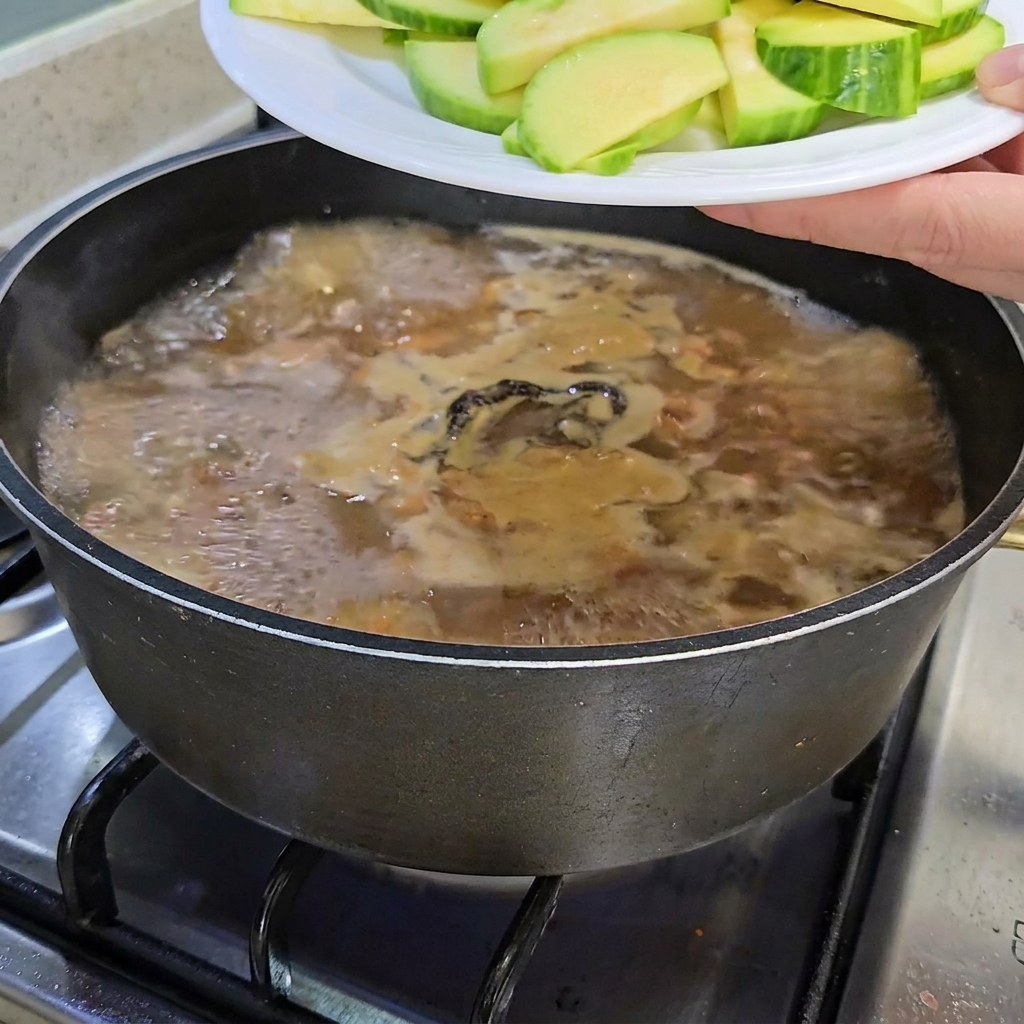Calabacín en rodajas y setas enoki siendo añadidos al estofado.