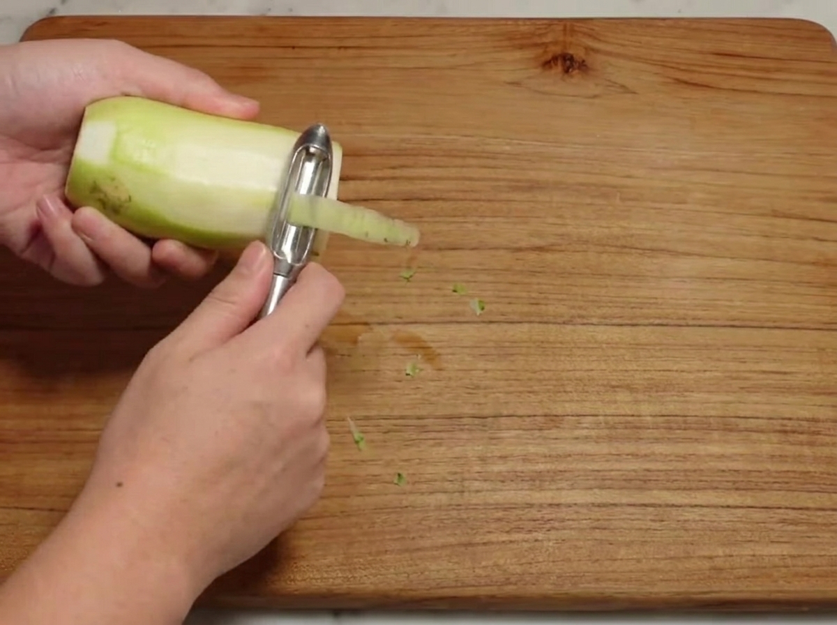 Un rábano blanco crudo siendo pelado sobre una tabla de madera.