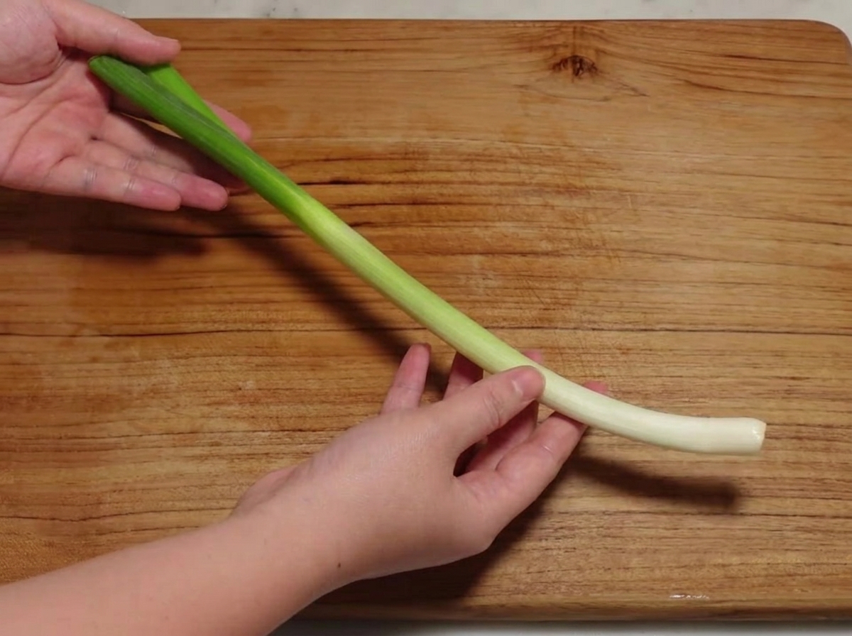 Una cebolleta siendo cortada en secciones diagonales sobre una tabla de madera.