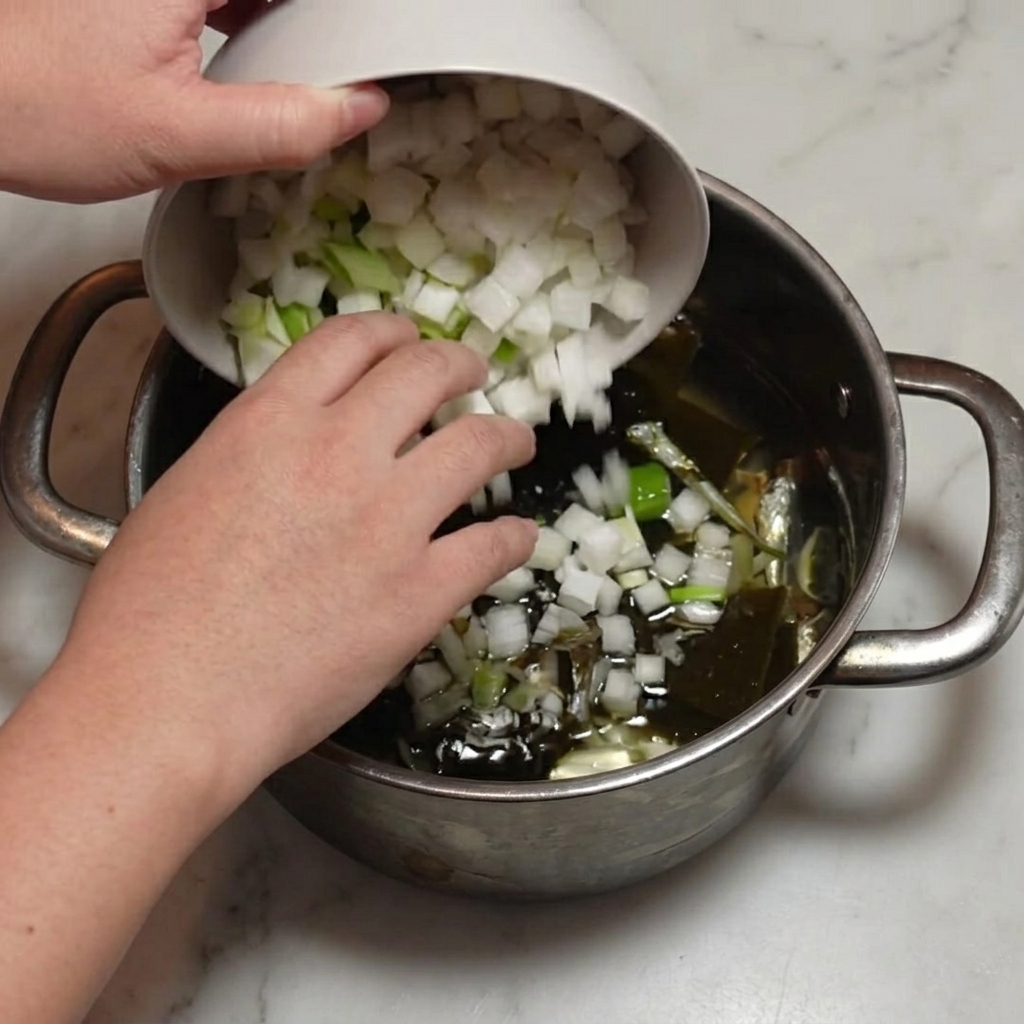 Rábano y cebolleta cortados siendo vertidos en la olla con anchoas y kombu.