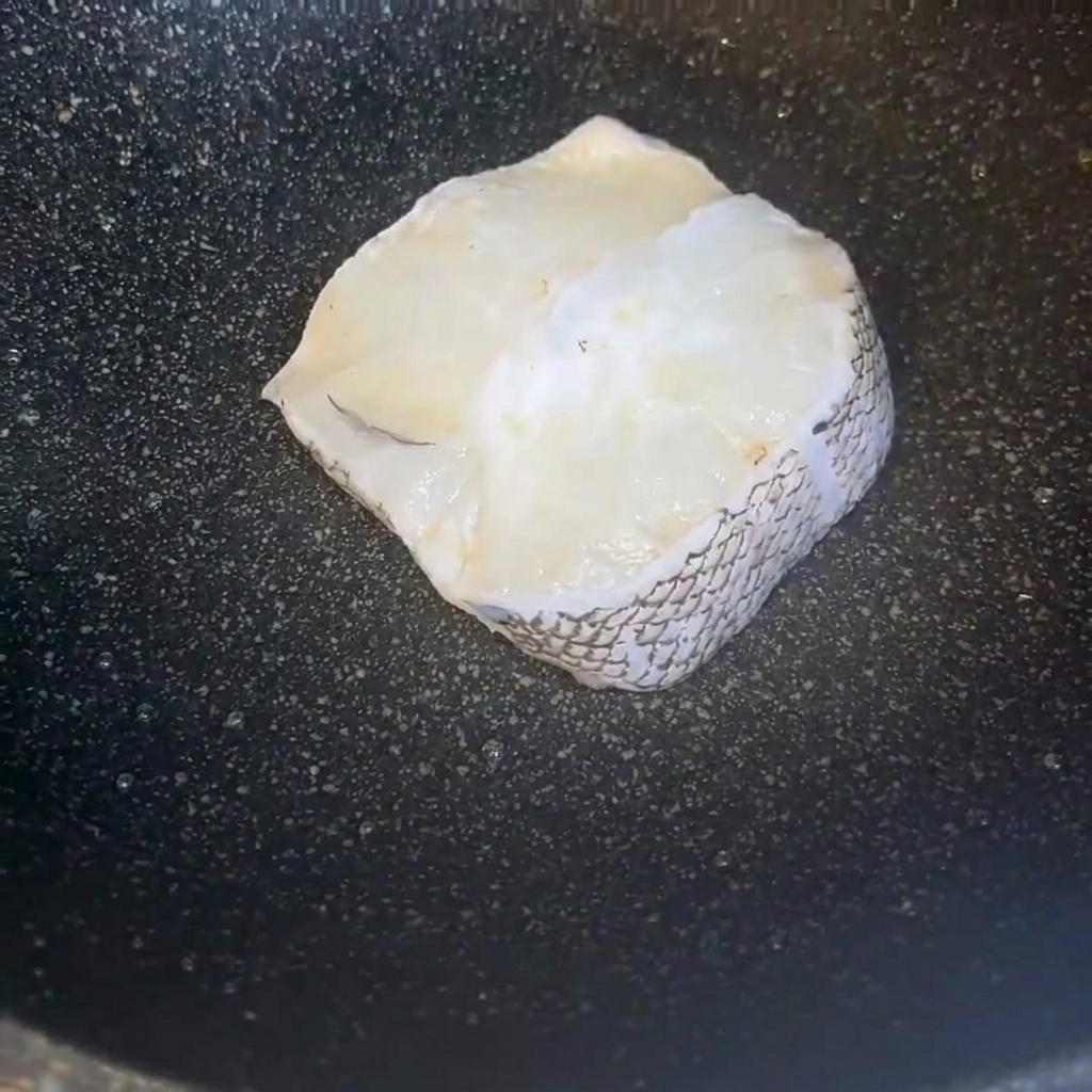 Trozos de filete de bacalao recién limpios dispuestos ordenadamente dentro de una sartén oscura.