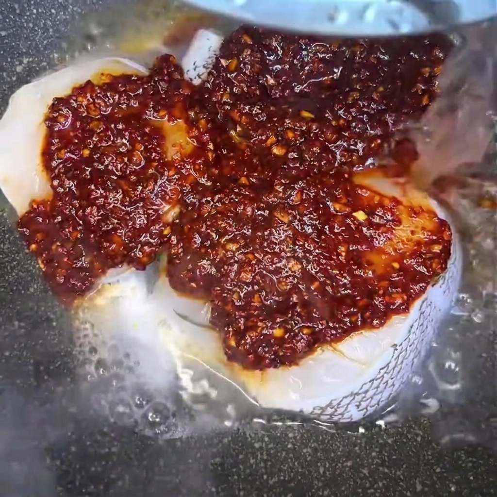 Agua vertiéndose en una sartén que contiene filetes de bacalao crudo sazonados, creando un líquido de estofado sabroso.