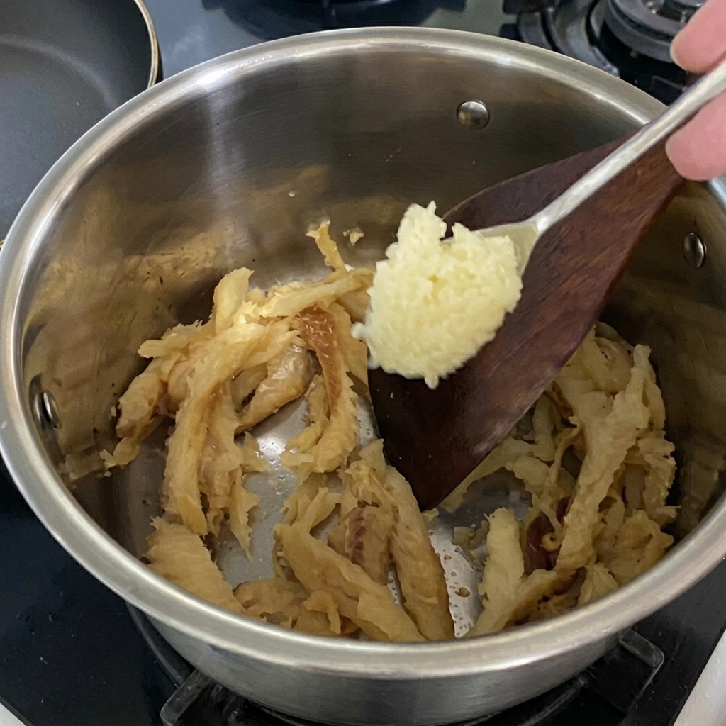 Una cucharada de ajo picado siendo añadida al abadejo amarillo en la olla.