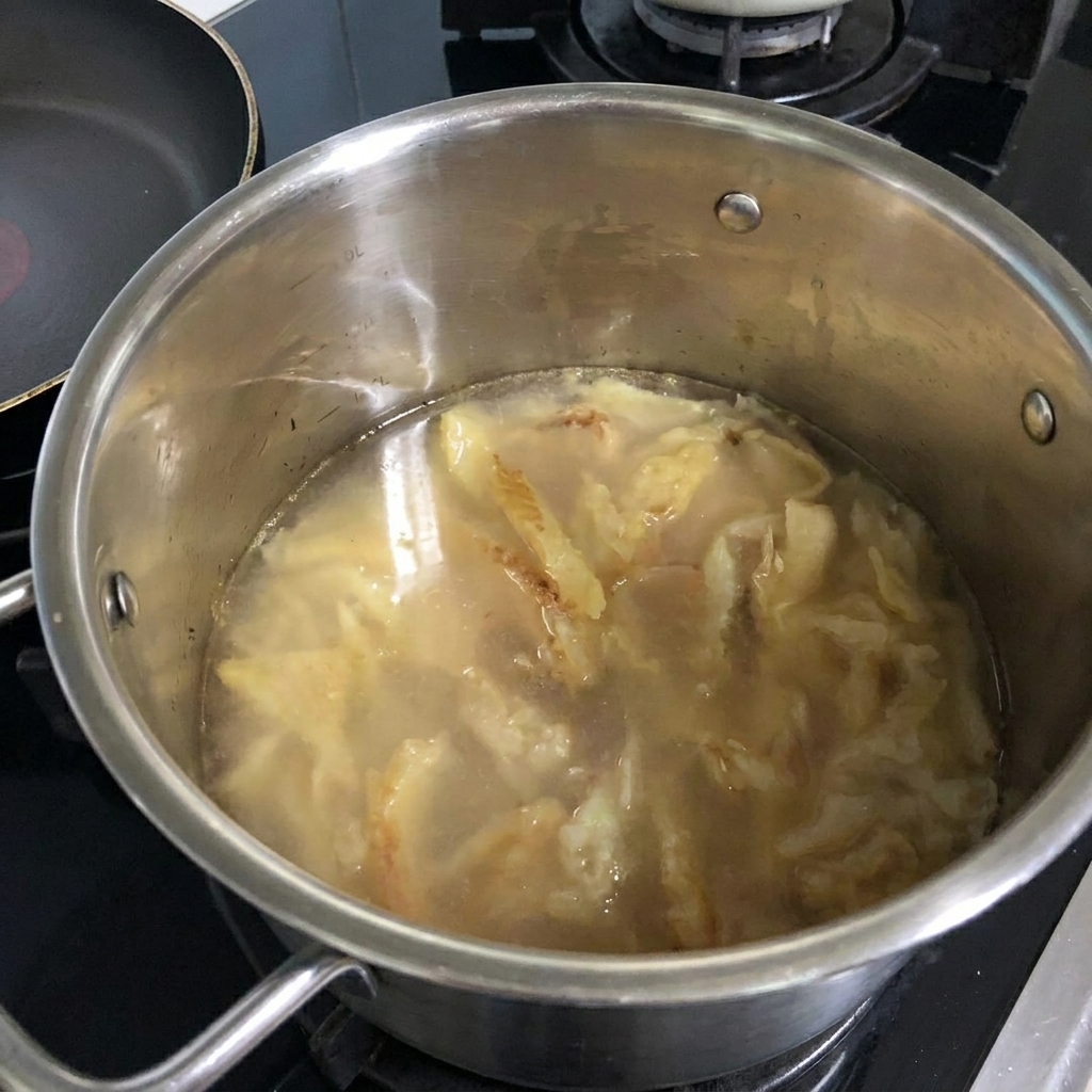 Agua siendo vertida de una botella a la olla que contiene el abadejo sofrito.