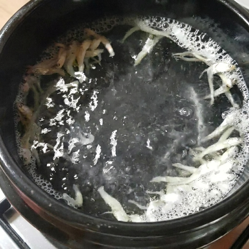 Una olla de piedra negra con agua, anchoas secas y alga kelp hirviendo en la estufa.