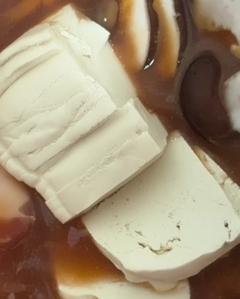 Láminas de tofu blanco siendo colocadas con cuidado en el estofado.