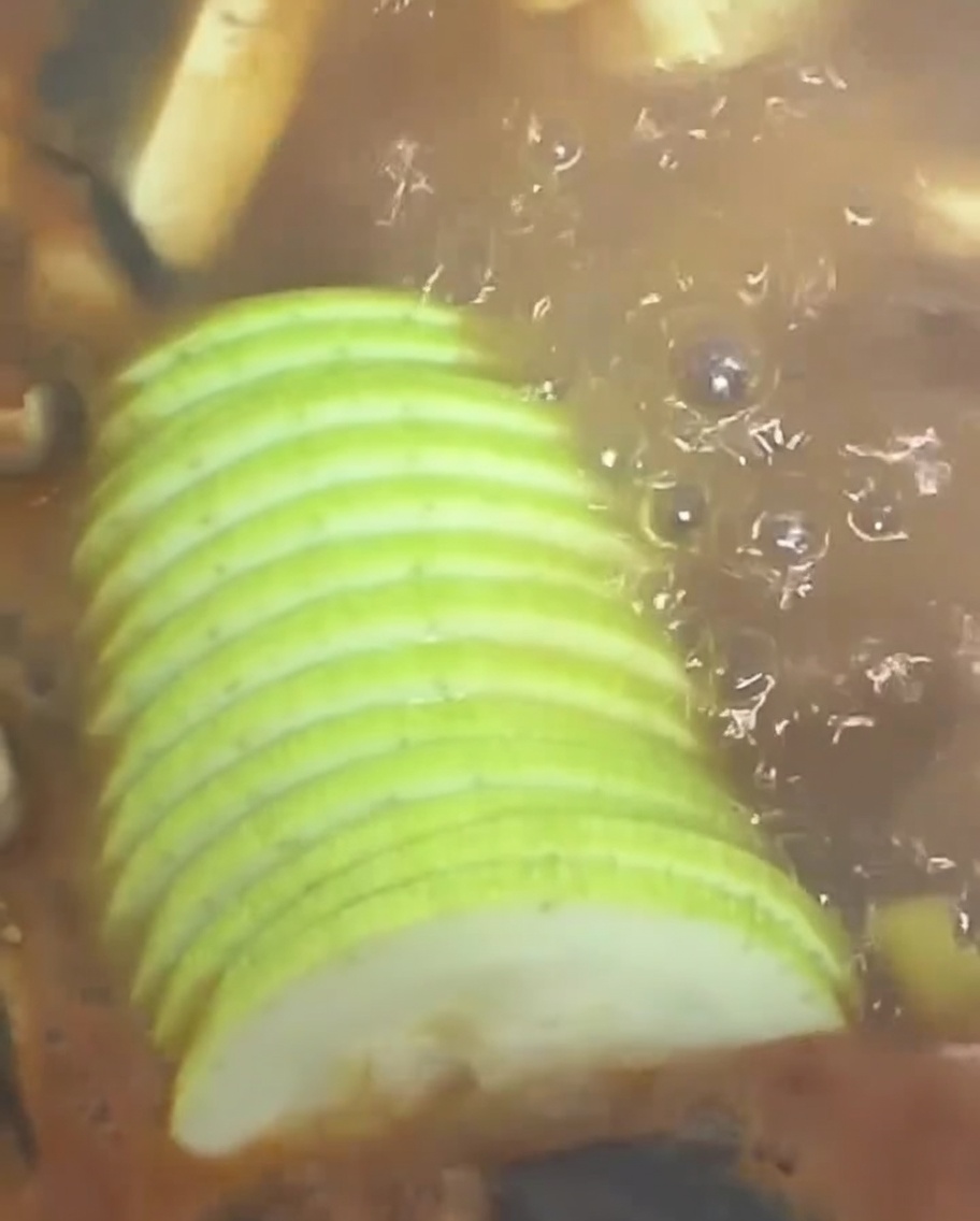 Láminas de calabacín verde siendo añadidas al estofado.