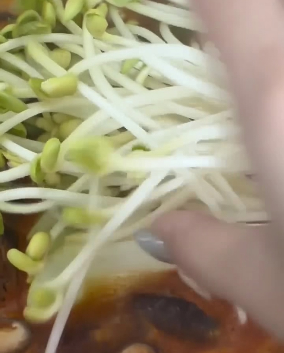 Un puñado de brotes de soja frescos siendo añadidos a la olla.
