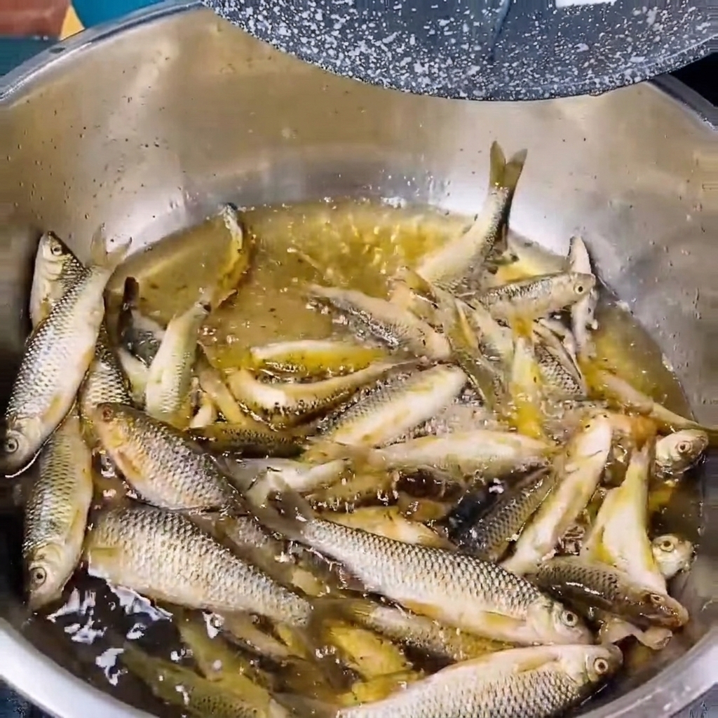 Pescaditos de río frescos siendo enjuagados en un cuenco metálico con agua clara.