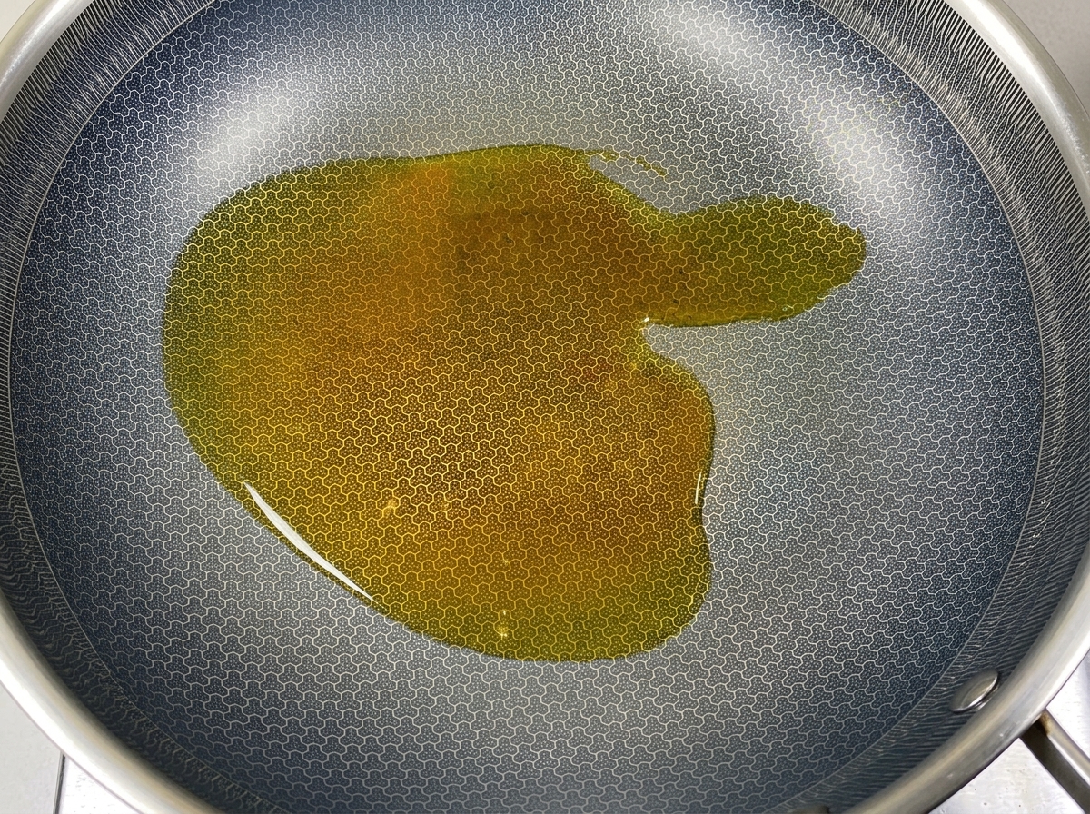 Un trozo de manteca de cerdo sólida derritiéndose en aceite caliente dentro de un wok texturizado.