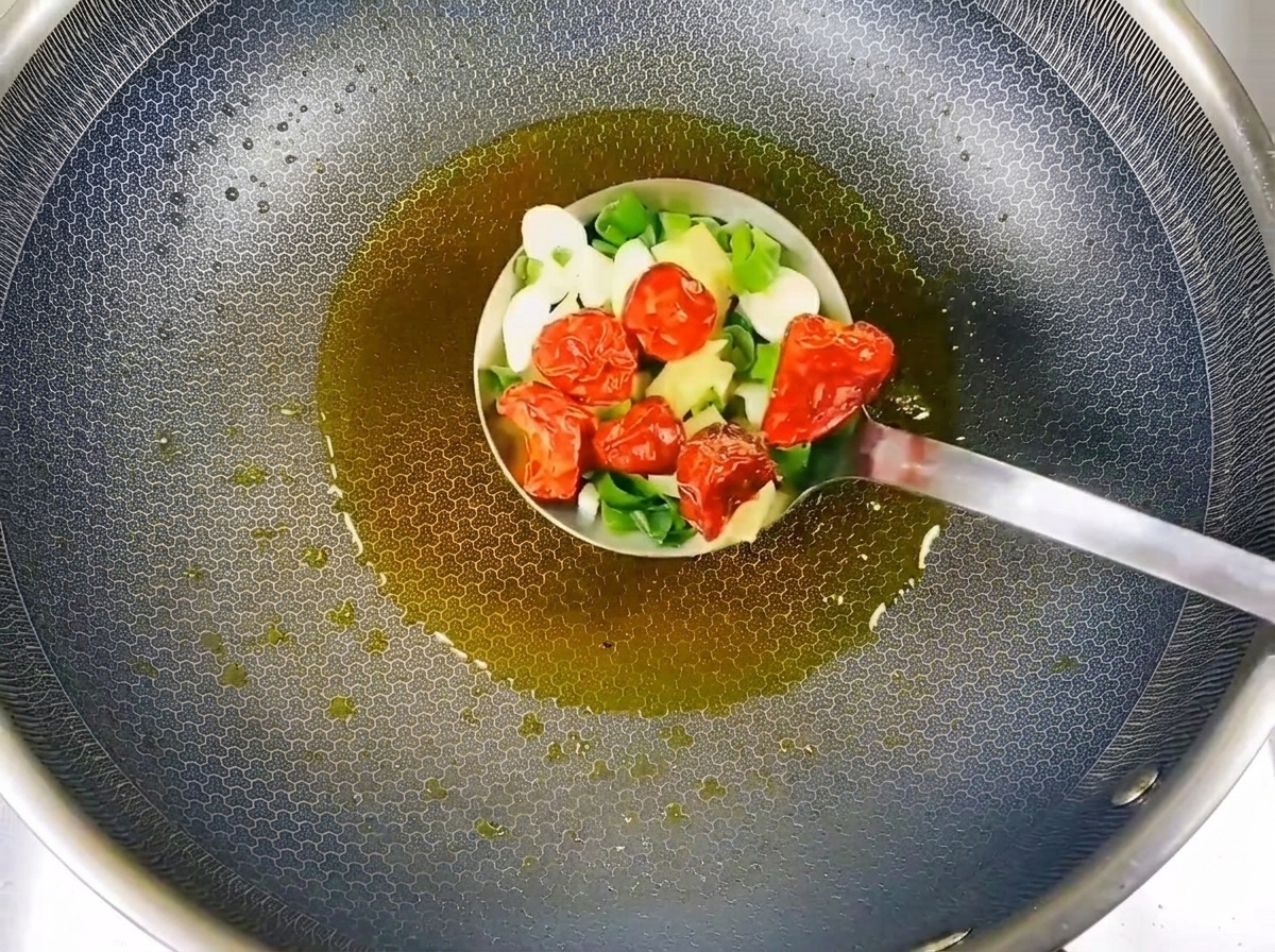 Cebollinos picados, láminas de ajo y chiles rojos secos siendo salteados en aceite caliente.