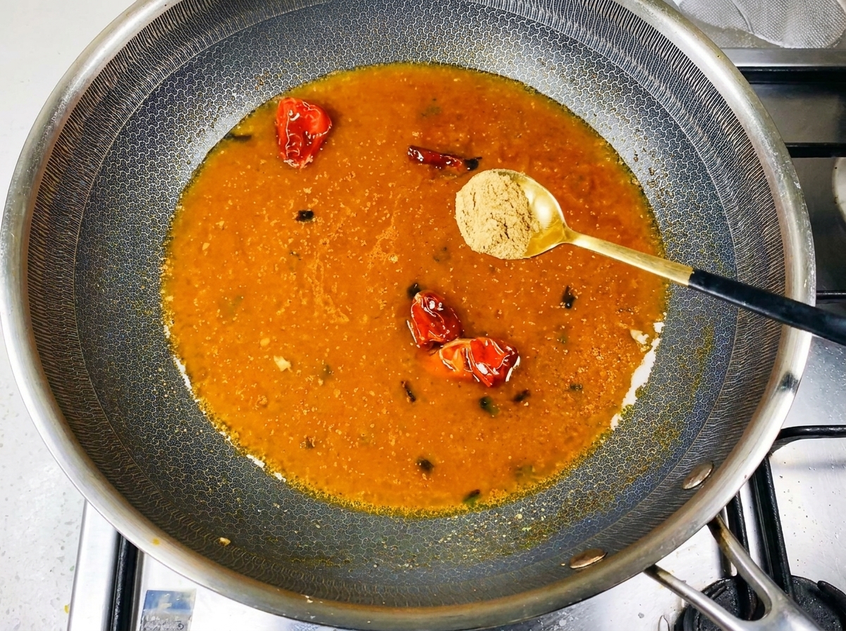 Especias en polvo siendo espolvoreadas sobre un caldo naranja a fuego lento en el wok.