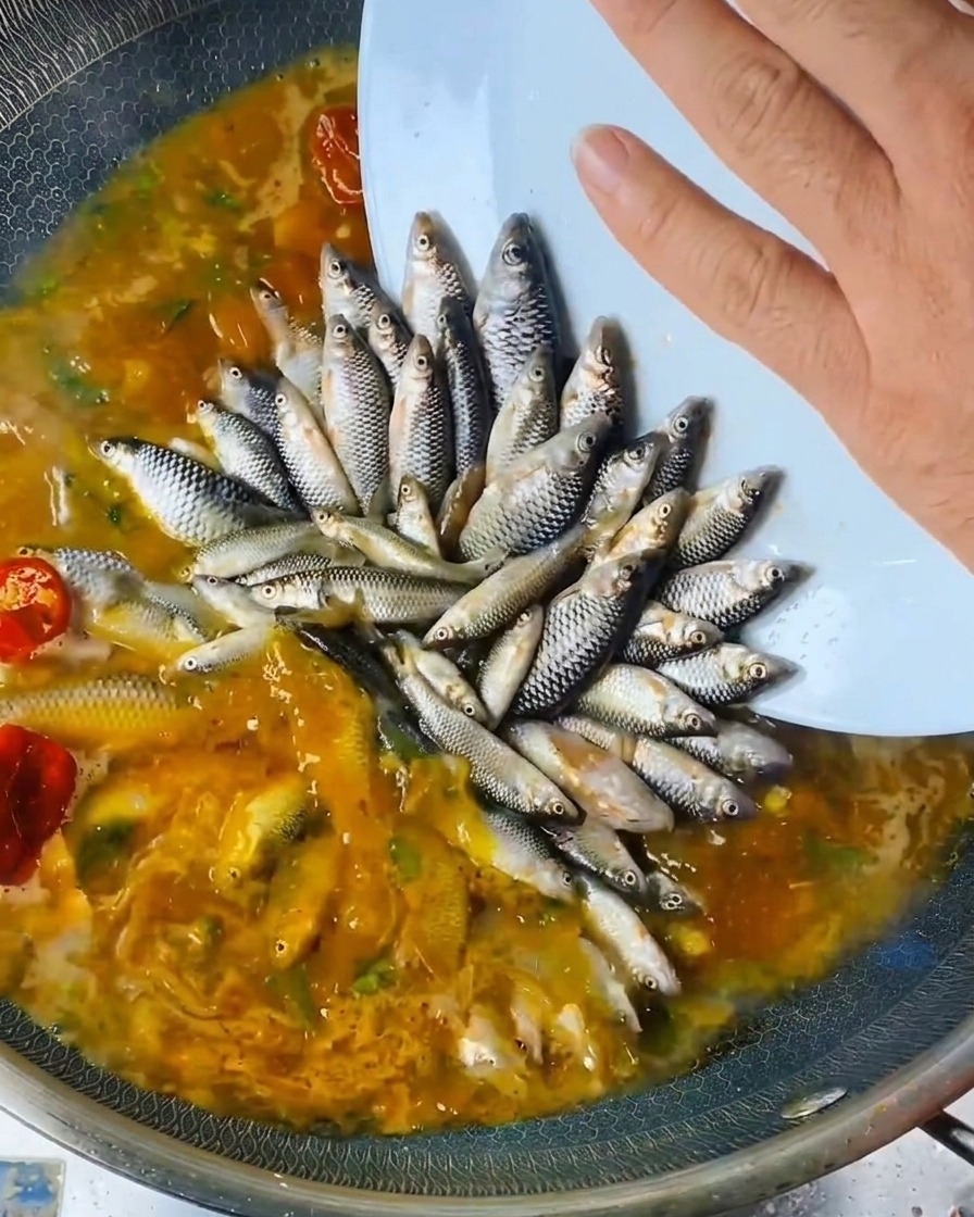 Una mano vertiendo aliño líquido desde una botella sobre el pescado en el wok.