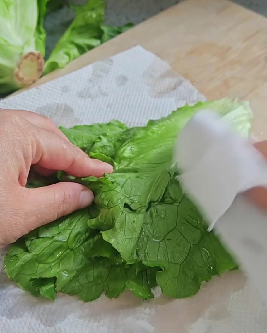 Manos secando hojas de lechuga fresca con papel de cocina.