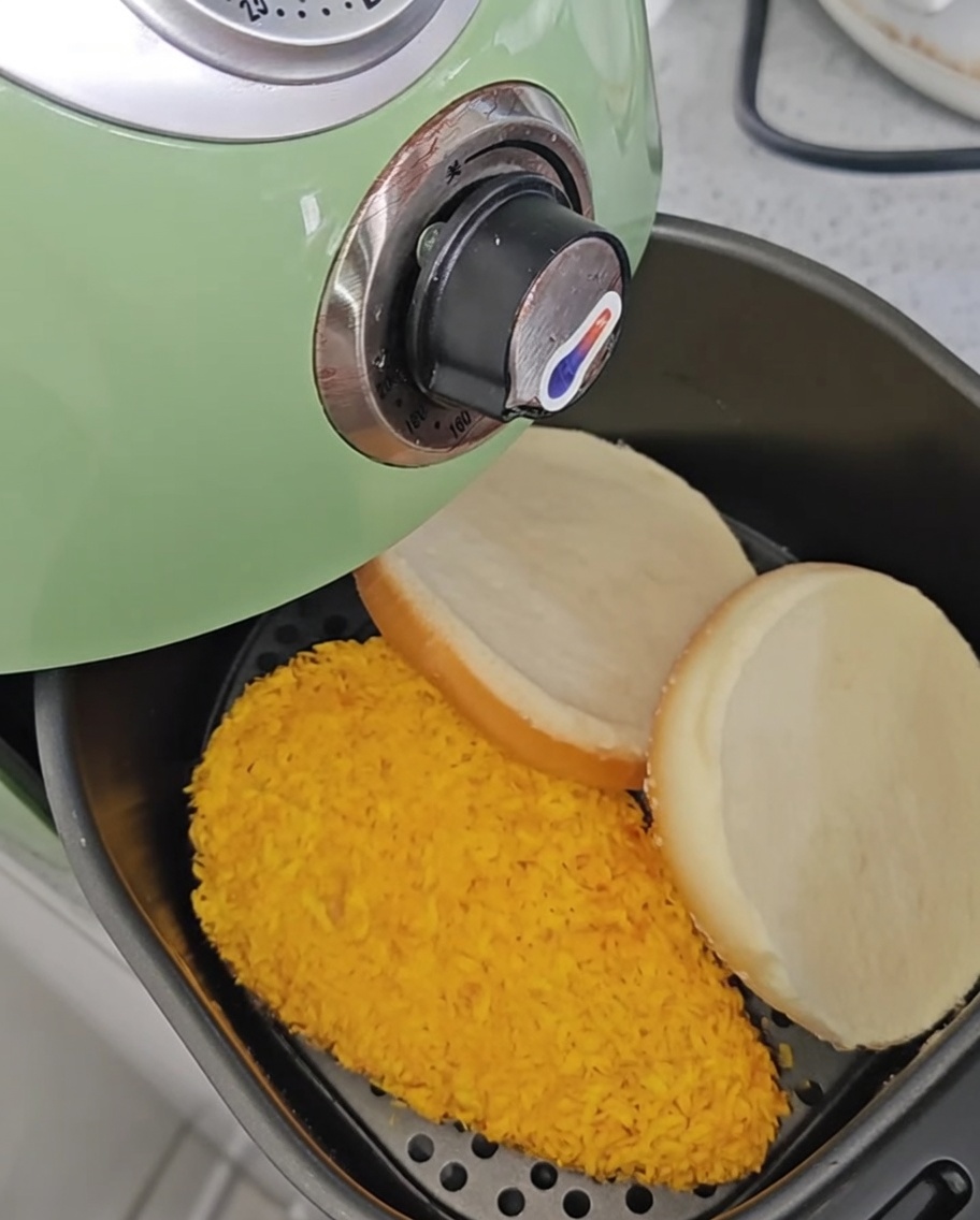 Filetes de pollo dentro de la freidora tras darles la vuelta, con los panes de hamburguesa al lado.