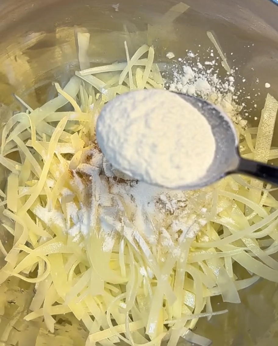Bol de patatas ralladas siendo cubiertas con una mezcla de harina y almidón de maíz.