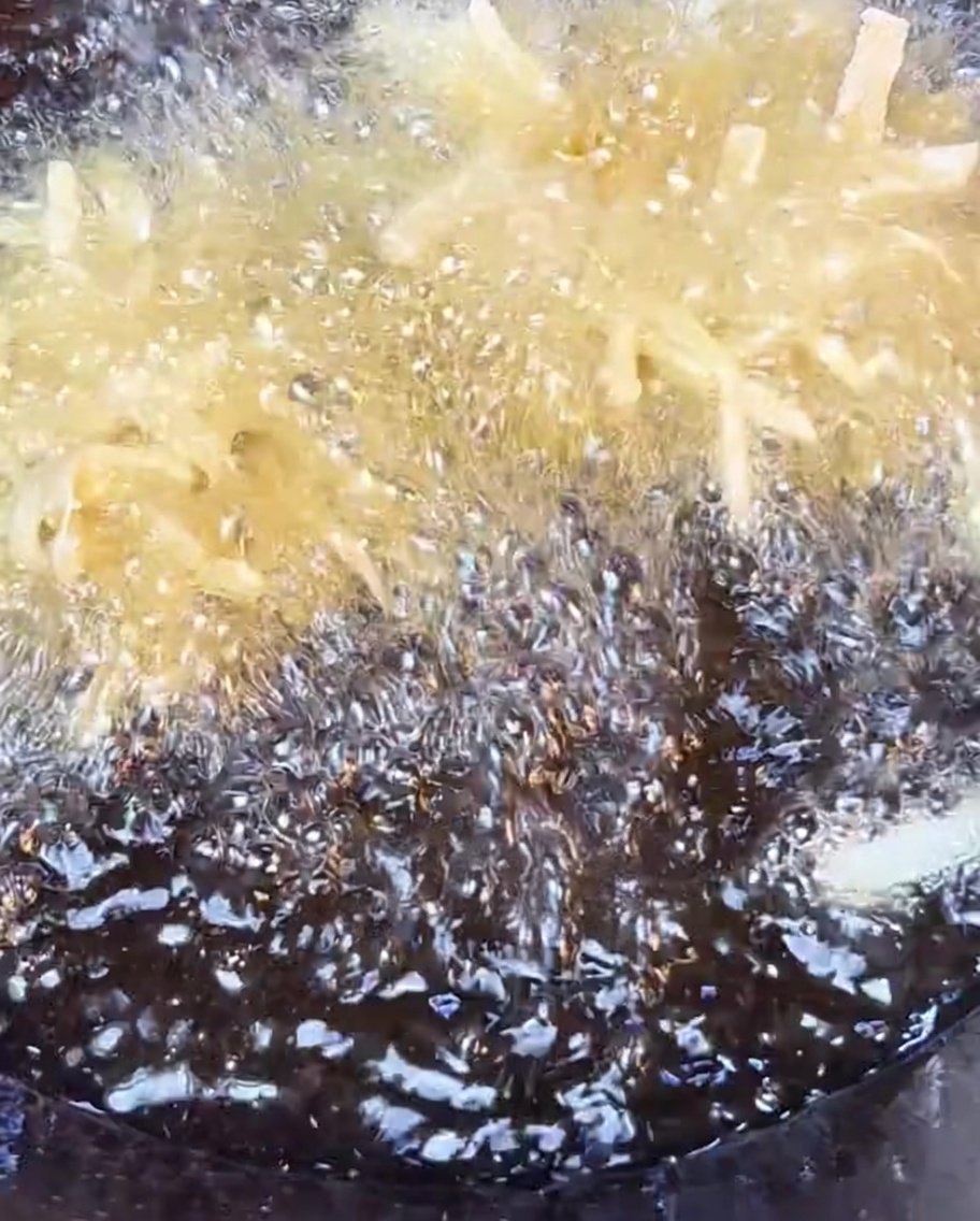 Patatas ralladas crujientes friéndose en aceite caliente hasta quedar doradas.