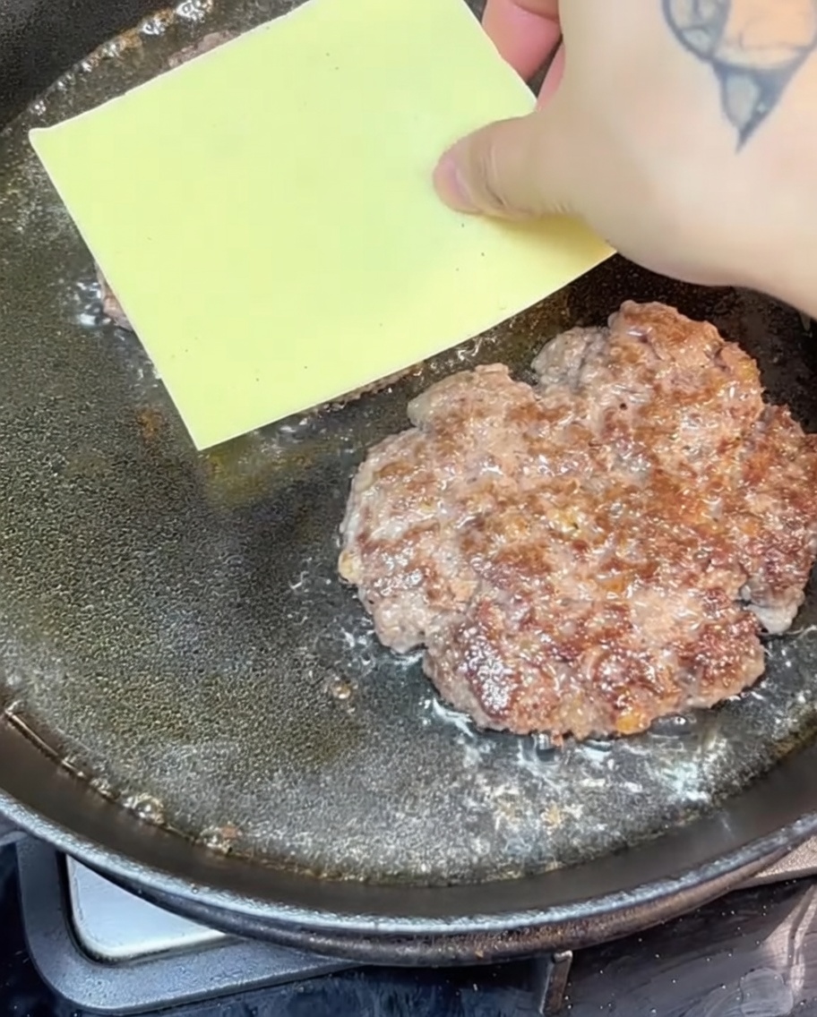 Hamburguesas de ternera con queso chisporroteando en una sartén de hierro fundido.