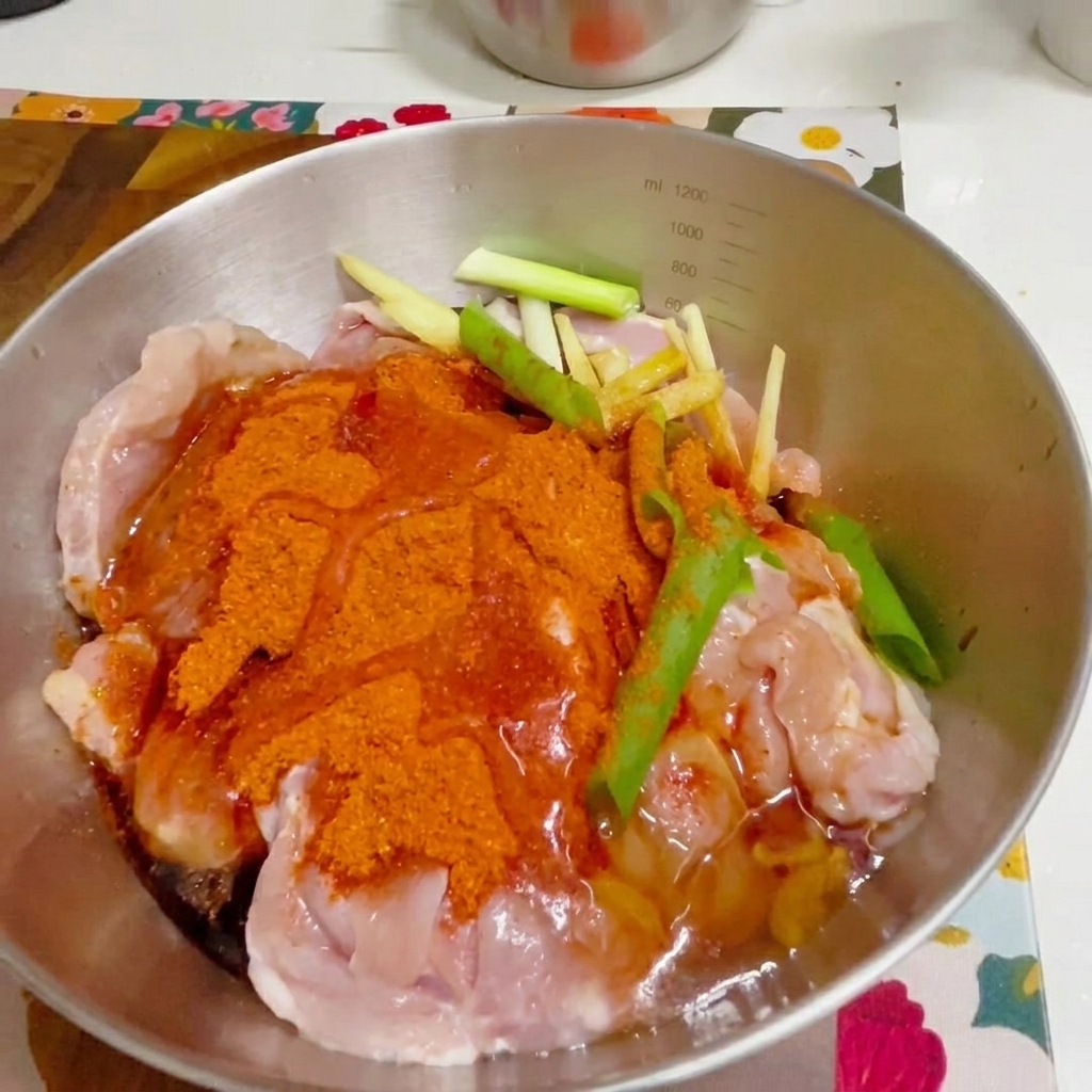 Una mano con guante mezclando el pollo sazonado en un bol de metal.