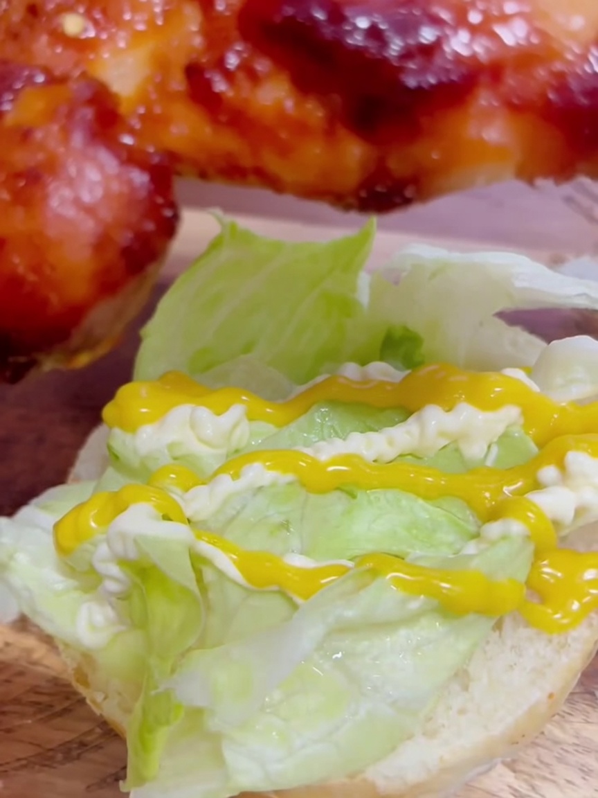 Un trozo de muslo de pollo teriyaki glaseado colocándose sobre la lechuga aliñada con mostaza con miel y mayonesa.